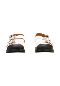 Sandales en cuir blanc avec doubles brides à boucles argentées et semelles plates noires, vues de face sur un fond blanc.