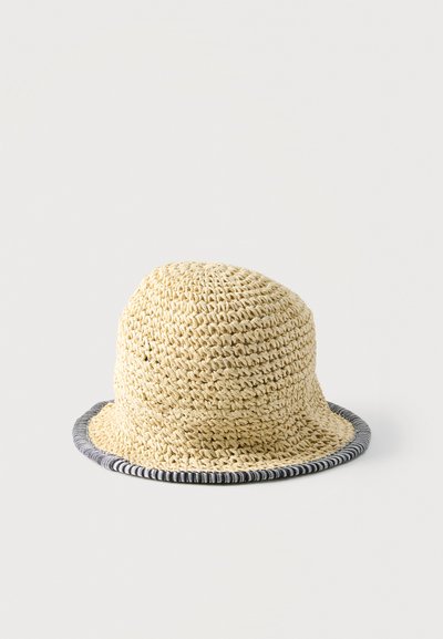 Chapeau bob beige en crochet avec un bord légèrement évasé, bordé d'une garniture rayée noir et blanc, sur un fond clair uni.