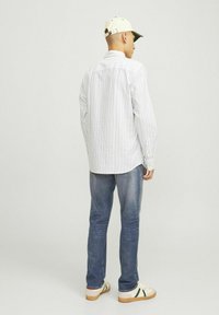 Camisa de manga larga a rayas en blanco y azul, combinada con jeans azul desgastados y zapatillas blancas con detalles verdes. Gorra de color claro llevada.