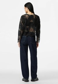 Černý krajkový top s dlouhými rukávy a otevřenými zády, v kombinaci s tmavě modrými širokými džíny a černými teniskami. Detailní květinový vzor.
