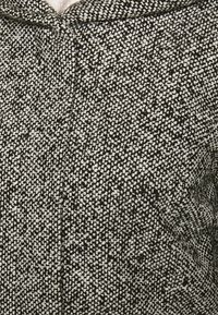 Tejido texturizado en blanco y negro con un patrón moteado, que presenta una apariencia suave y tejida, y un diseño con capucha.