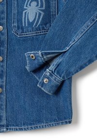 Denim jack in medium blauw met een spinnenafbeelding op de borstzak, voorzien van metalen drukknoopsluitingen en details op de manchetten.
