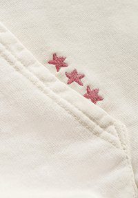 Kremowa tkanina o teksturowanym wykończeniu z trzema różowymi haftowanymi gwiazdkami w pobliżu szwu, podkreślającymi szczegół projektu.