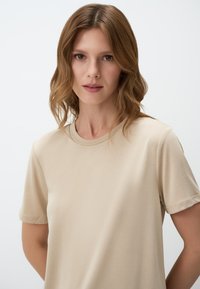 Beige t-shirt met korte mouwen en een ronde hals, gemaakt van zachte stof, met een gladde textuur en minimalistische ontwerpdetails.