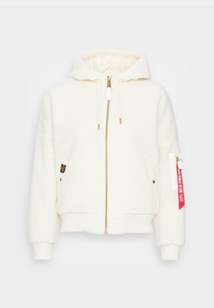 Haut de sweat à capuche zippé en polaire blanche avec une capuche doublée, des poignets et un ourlet côtelés. Comprend une fermeture éclair dorée, des poches avant et une étiquette en tissu rouge sur la manche.