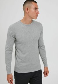 Suéter gris de manga larga hecho de una tela suave, con cuello redondo y puños y dobladillo acanalados, llevado por un hombre.