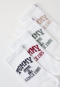 Witte katoen sokken met ribbeltextuur. Elke paar toont "TOMMY" en "SINCE 1985" in verschillende kleuren: donkerblauw, groen en rood.