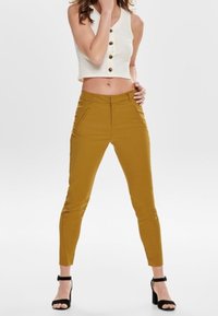 Geel aangesloten broek met een gladde textuur en zijzakken, gecombineerd met een witte cropped top met knopen aan de voorkant en een hoge halslijn.