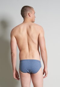 Culotte bleue en tricot avec une texture douce, taille élastique et design ajusté, présentée de dos, sur un modèle masculin à la peau nue.