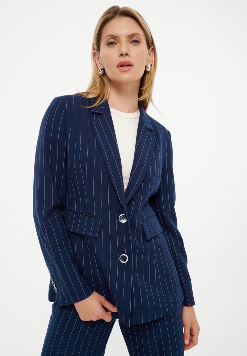 Blazer de rayas marinas con dos botones, diseño de un solo botón, solapas con muesca y bolsillos laterales. Textura de tela suave.