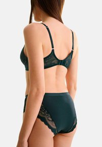 Soutien-gorge en dentelle vert foncé et ensemble de culottes taille haute. Tissu doux avec des accents en dentelle à bords festonnés sur les côtés. Bretelles ajustables et fermeture à crochets à l'arrière.