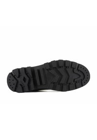Suela de goma negra con profundos surcos, que presenta una combinación de patrones horizontales y diagonales para mejorar el agarre y la tracción.