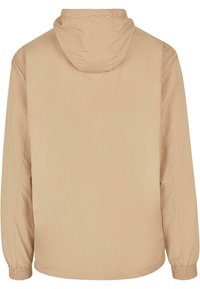 Beige letvægtsjakke med hætte, elastiske manchetter og en glat tekstur. Har et enkelt design uden synligt hardware eller lommer.