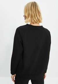 Schwarzer Sweatshirt mit Rundhalsausschnitt, langen Raglanärmeln und gerippten Bündchen. Weicher Stoff, minimalistisches Design ohne Muster oder Akzente.