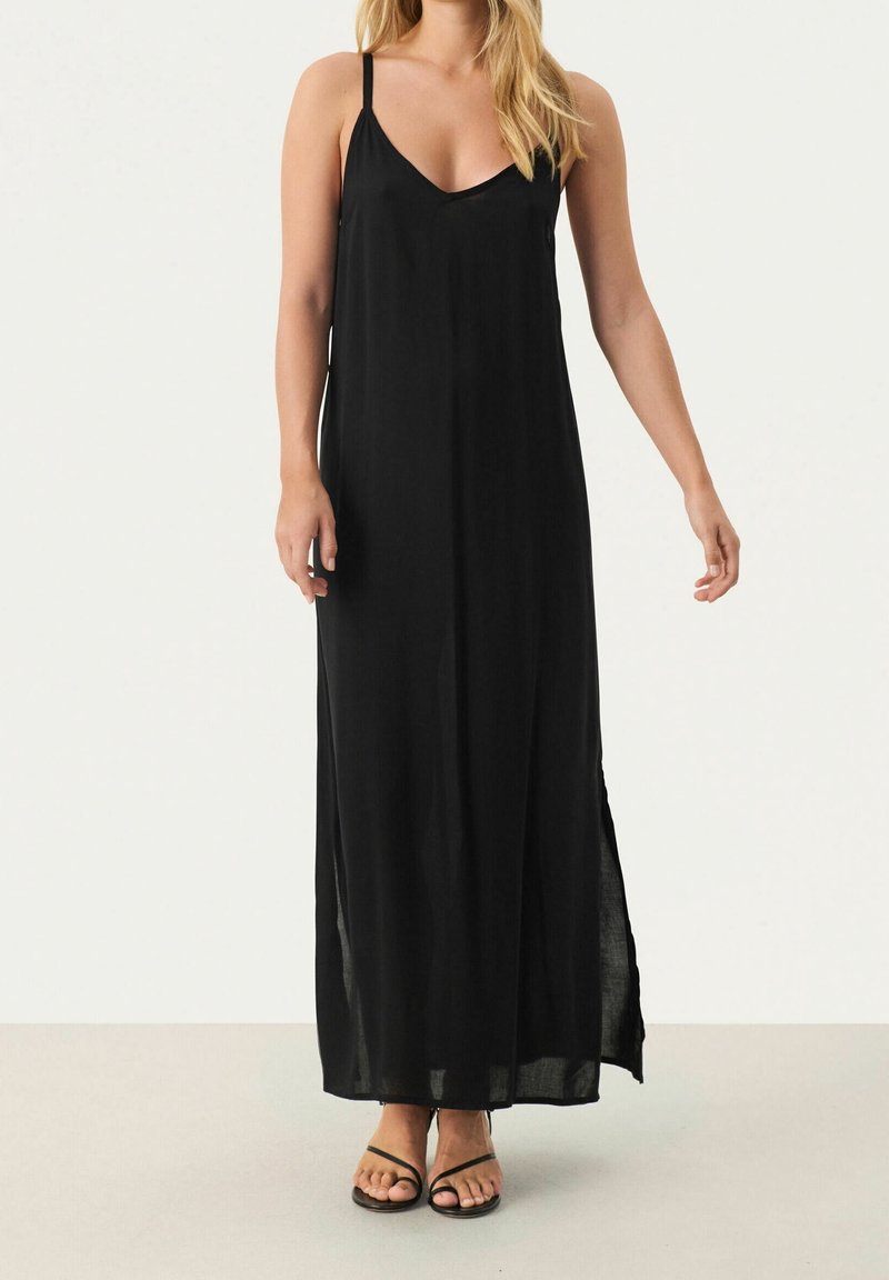 Schwarzes Maxikleid mit dünnen Trägern, V-Ausschnitt und seitlichen Schlitzen. Aus leichtem Stoff für ein fließendes Design. Flache schwarze Sandalen runden den Look ab.