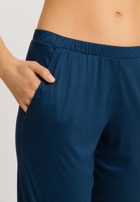 Pantalones azul marino con una textura suave, cinturilla elástica y bolsillos laterales. La tela tiene un ligero brillo, mostrada con una mano en un bolsillo.
