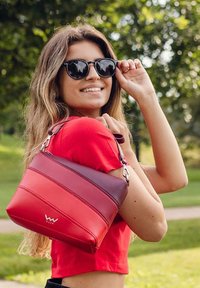 Červená a vínová kabelka vyrobená z umělé kůže, s horizontálním pruhovaným designem a stříbrnými detaily. Vhodná pro každodenní nošení.