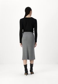 Top negro de manga larga, falda midi de canalé gris y botas negras hasta la rodilla. La falda se ajusta de manera ceñida, con una ligera abertura en un lado.