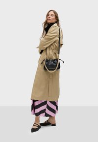 Beige trench coat with a belted waist, paired with a pink and black striped skirt. Accessories include a black bag with a chain strap and black shoes.