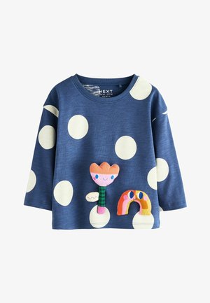 Cămașă albastră cu mâneci lungi, decorată cu buline albe mari. Prezintă un aplicat texturat în formă de floare și un curcubeu în culori vibrante. Design casual.