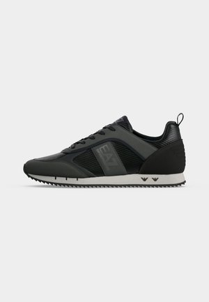 Baskets basses noires avec panneaux texturés, fermeture à lacets, semelle blanche crantée et marquage "EA7 Emporio Armani" sur le côté.