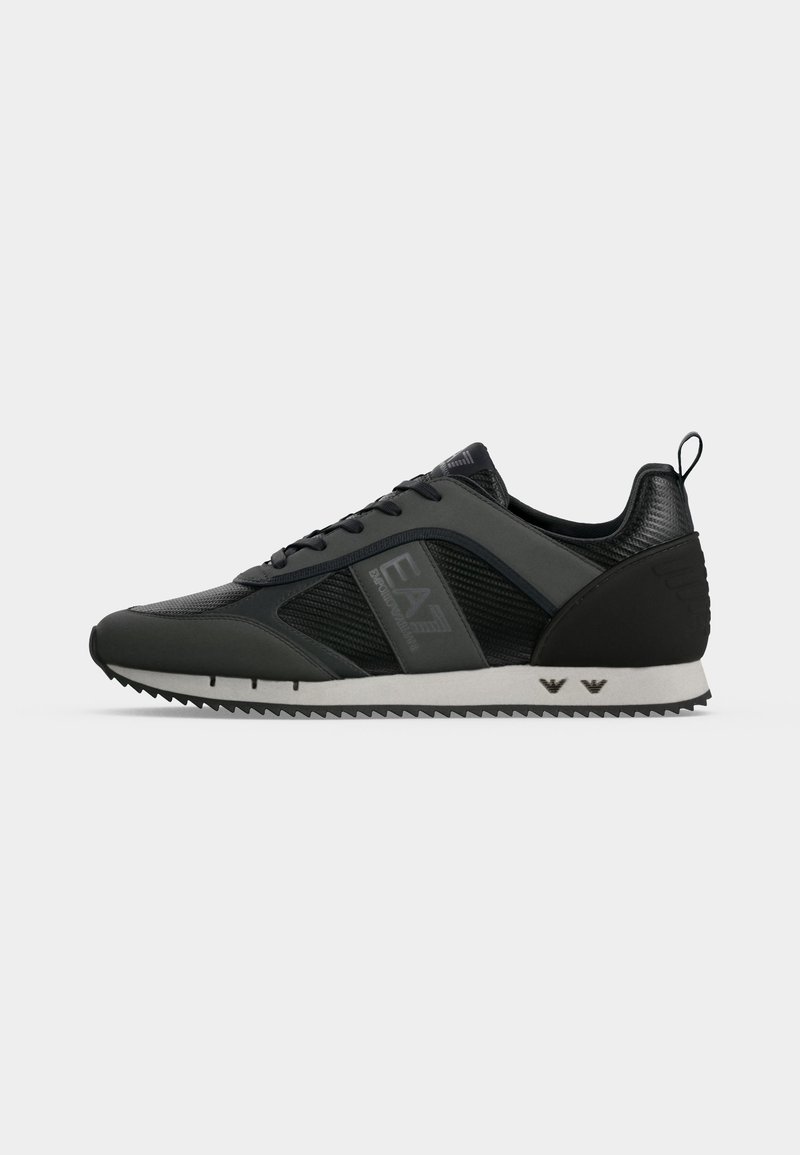 Baskets basses noires avec panneaux texturés, fermeture à lacets, semelle blanche crantée et marquage "EA7 Emporio Armani" sur le côté.