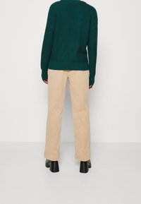 Pull vert tricoté avec manches larges et ourlet côtelé, associé à un pantalon beige à jambes droites et des chaussures noires à talons blocs.