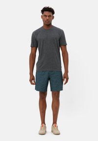 T-shirt gris à manches courtes, associé à un short bleu sarcelle. La tenue a une coupe décontractée et est complétée par des baskets beiges.