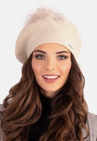 Fény bézs színű, texturált anyagból készült beret, a tetején egy bolyhos pom-pommal, az oldalán pedig egy kis fém logóval.