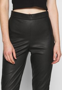 Czarne skórzane spodnie o gładkiej fakturze, dopasowanym kroju, wysokim stanem oraz detalach zamka błyskawicznego z boku, prezentujące staranne szwy.