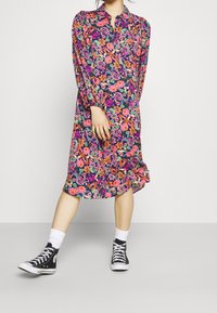 Robe florale avec un fond sombre, ornée de fleurs roses, oranges et vertes vives ; longueur genou, manches longues et col boutonné.