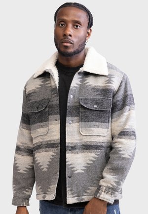 Gray and white patterned jacket with a fluffy collar, featuring front pockets and snap buttons, worn over a black T-shirt.