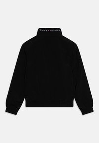 Sort bomberjakke med ribbet krave, elastiske manchetter og talje. Har et logo på kraven. Stoffet virker glat og let blankt.