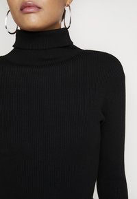 Czarny sweter z wysokim kołnierzem, o dopasowanym kroju, z długimi rękawami, wykonany z teksturowanego, elastycznego materiału.
