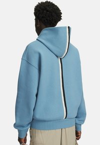 Lys blå pullover hoodie med en front kangaroo lomme, ribbet kant og sort-hvide lodrette striber på ryggen.