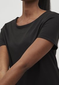 Svart kortärmad t-shirt med rund halsringning, tillverkad av mjukt bomullsmaterial. Visar axlarna och övre delen av armarna.