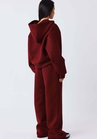 Bordeauxrode hoodie en bijpassende wijde broek van zacht materiaal, met een grote capuchon en een ontspannen pasvorm met minimale naden.
