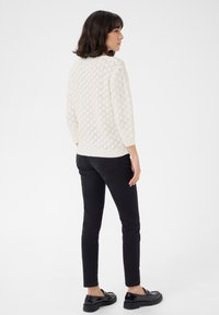 Pull crème tricoté avec motif en losanges, manches trois-quarts, associé à un pantalon slim noir et des mocassins noirs brillants.