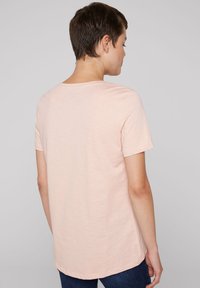 Koszulka z krótkim rękawem w jasnym brzoskwiniowym kolorze, z okrągłym dekoltem i prostym wykończeniem dołem. Wykonana z miękkiej, lekkiej tkaniny, z delikatną strukturą.