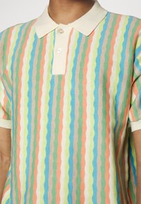 Randig polo t-shirt i pastellfärger – rosa, grön, blå och krämfärgad med en texturerad yta. Har krage och korta ärmar.