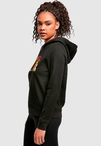Hoodie noir avec une poche kangourou, fermeture à cordon de serrage et impression graphique sur le devant. Matière en mélange de coton, texture douce, coupe décontractée.