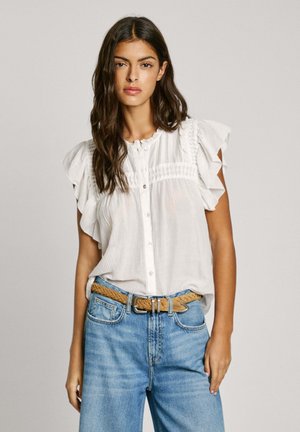 Weißes, kurzärmliges Bluse mit Rüschendetails, ausgestattet mit einer durchgehenden Knopfleiste und gerafften Akzenten, kombiniert mit hellblauen Denim-Jeans und einem geflochtenen Gürtel.