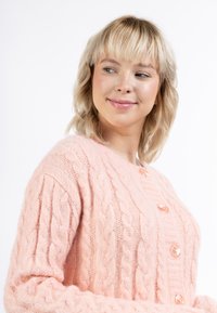 Rosa kabelstickad cardigan med v-ringning, långa ärmar och runda knappar. Mjuk, texturerad tyg med framträdande stickade mönster.