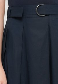 Navy blue skirt with a belt featuring a circular silver buckle, pleated design, and smooth texture. Tailored, mid-length cut.