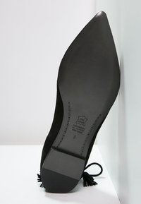 Zapato de cuero negro con punta afilada y tacón delgado. Presenta un upper texturizado y una suela negra lisa con detalles de marca.