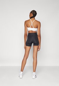 White sports bra with crisscross back straps paired with black high-waisted shorts. Model wears white sneakers, hair in braids.