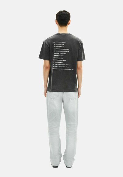 Juodas trumpomis rankovėmis marškinėliai su baltu tekstu ant nugaros, derinami su šviesiai pilkomis džinsomis. Audinys atrodo švelnus ir su laisvu prigludimu.