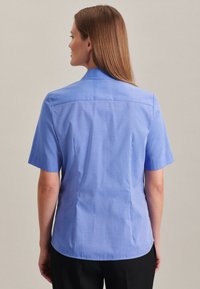 Camicia azzurro chiaro a maniche corte con colletto strutturato, tessuto liscio e sottile texture; vestibilità su misura con cuciture laterali.