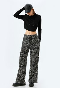 Zwarte cropped hoodie met trekkoorden, gecombineerd met brede broekspijpen met een zwart-wit gespoten patroon en zijzakken. Zwarte schoenen inbegrepen.
