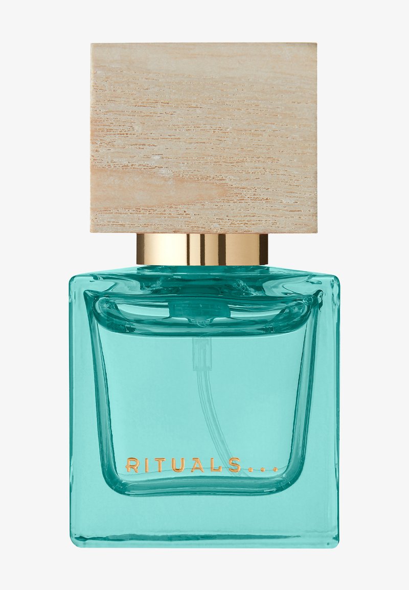 Bouteille de parfum en verre transparent avec un liquide turquoise, dotée d'un capuchon doré et d'un couvercle en bois texturé. L'étiquette indique "RITUALS..." en doré.